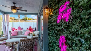 Un patio al aire libre con mobiliario de mimbre, ventilador de techo y letrero de neón.