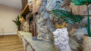 Un muro de piedra con una planta decorativa, un jarrón alto y una estatua de león con corona.