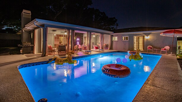 Una piscina con juguetes inflables, un porche cubierto y una casa con garaje visible.
