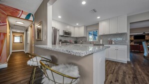 Una cocina moderna con armarios blancos, encimera de granito y una isla central con taburetes de bar.