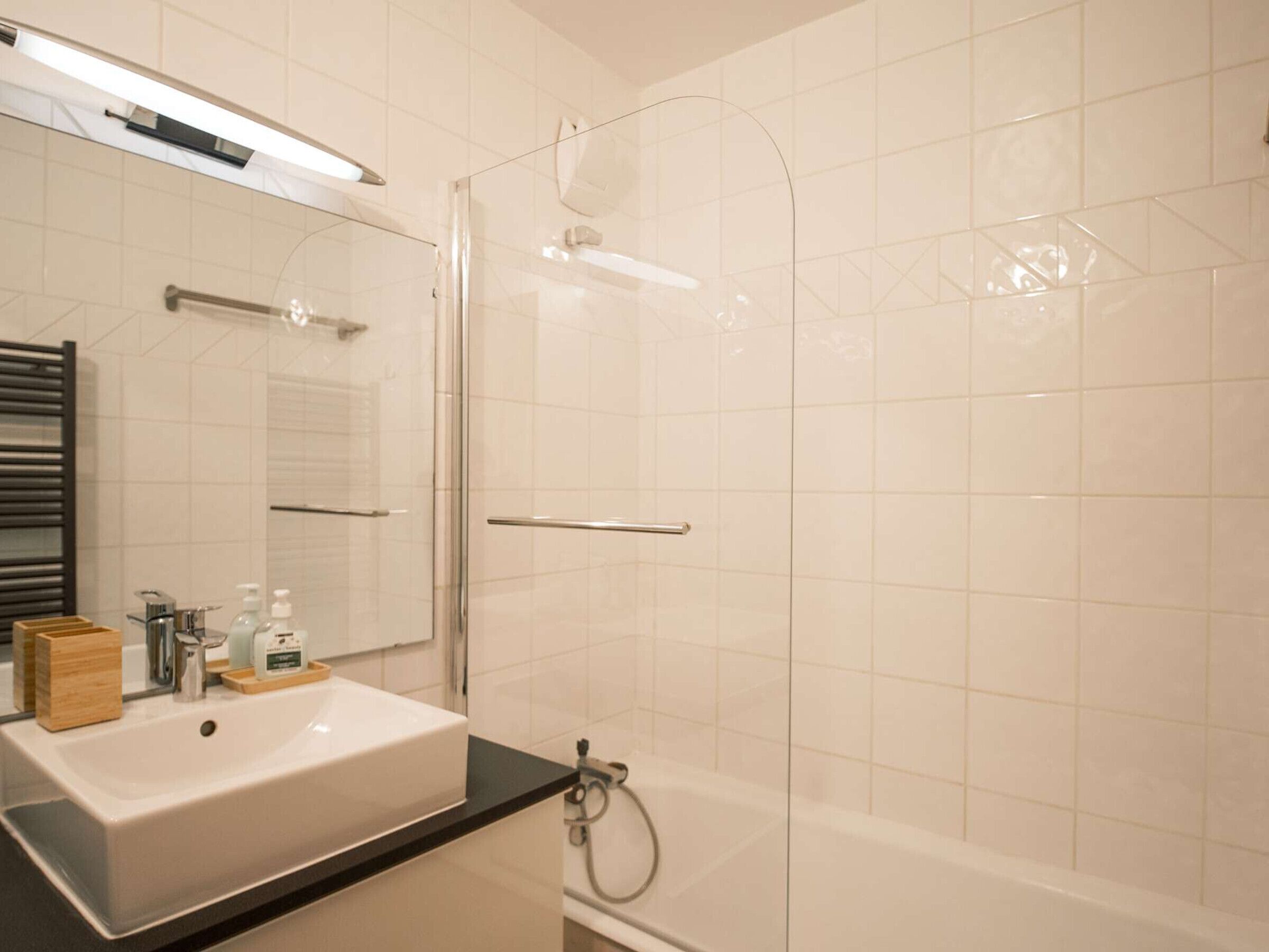 A modern bathroom with a white sink, a glass shower enclosure, and a black countertop.
