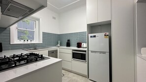 A modern kitchen with white cabinets, a gas stove, a microwave, and a refrigerator.