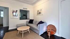 A modern living room with a sofa, a round table, and a coffee table. There are two paintings on the wall and a sign that reads "MANLY".