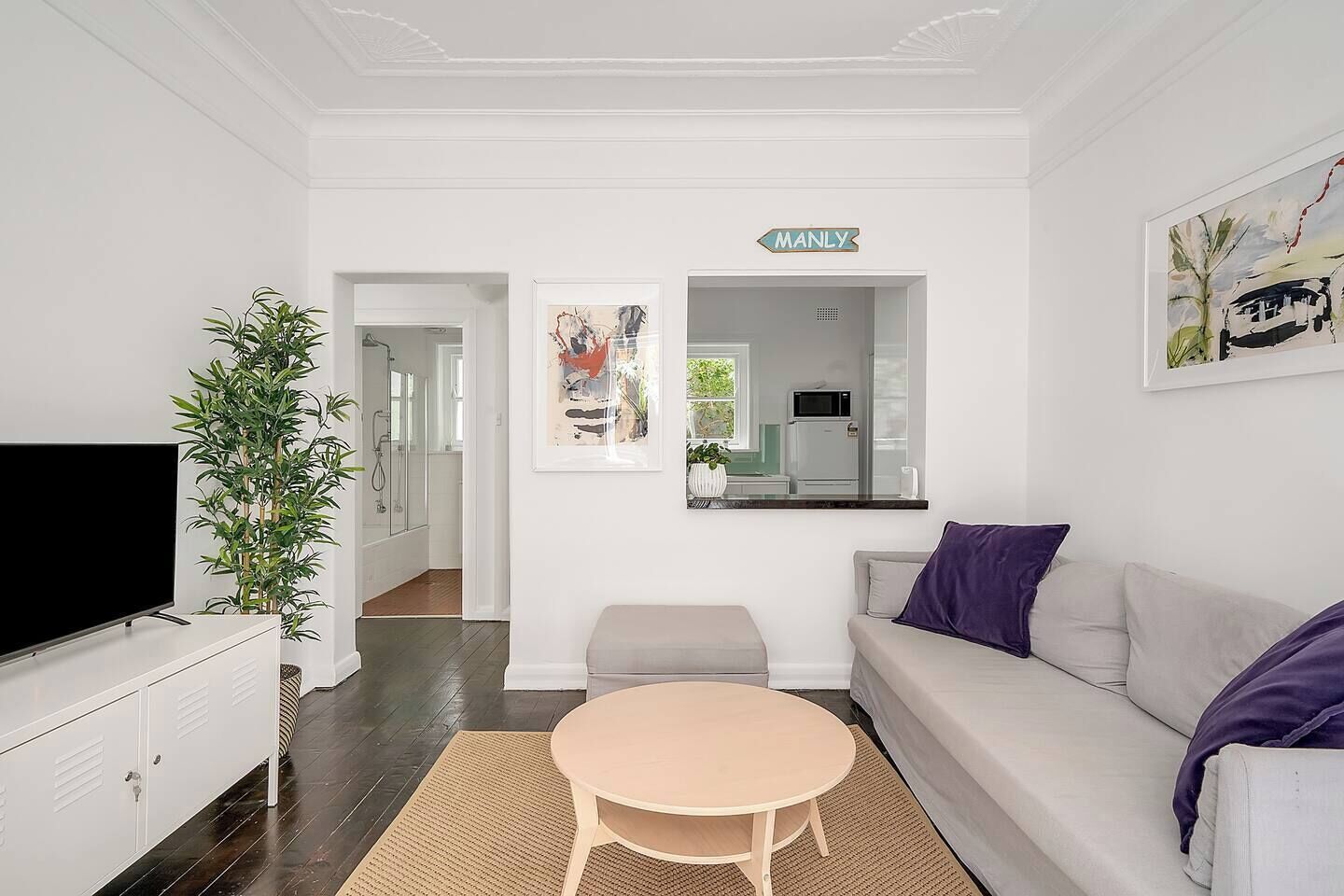 A modern living room with a flat-screen TV, a sofa, a coffee table, and a potted plant.