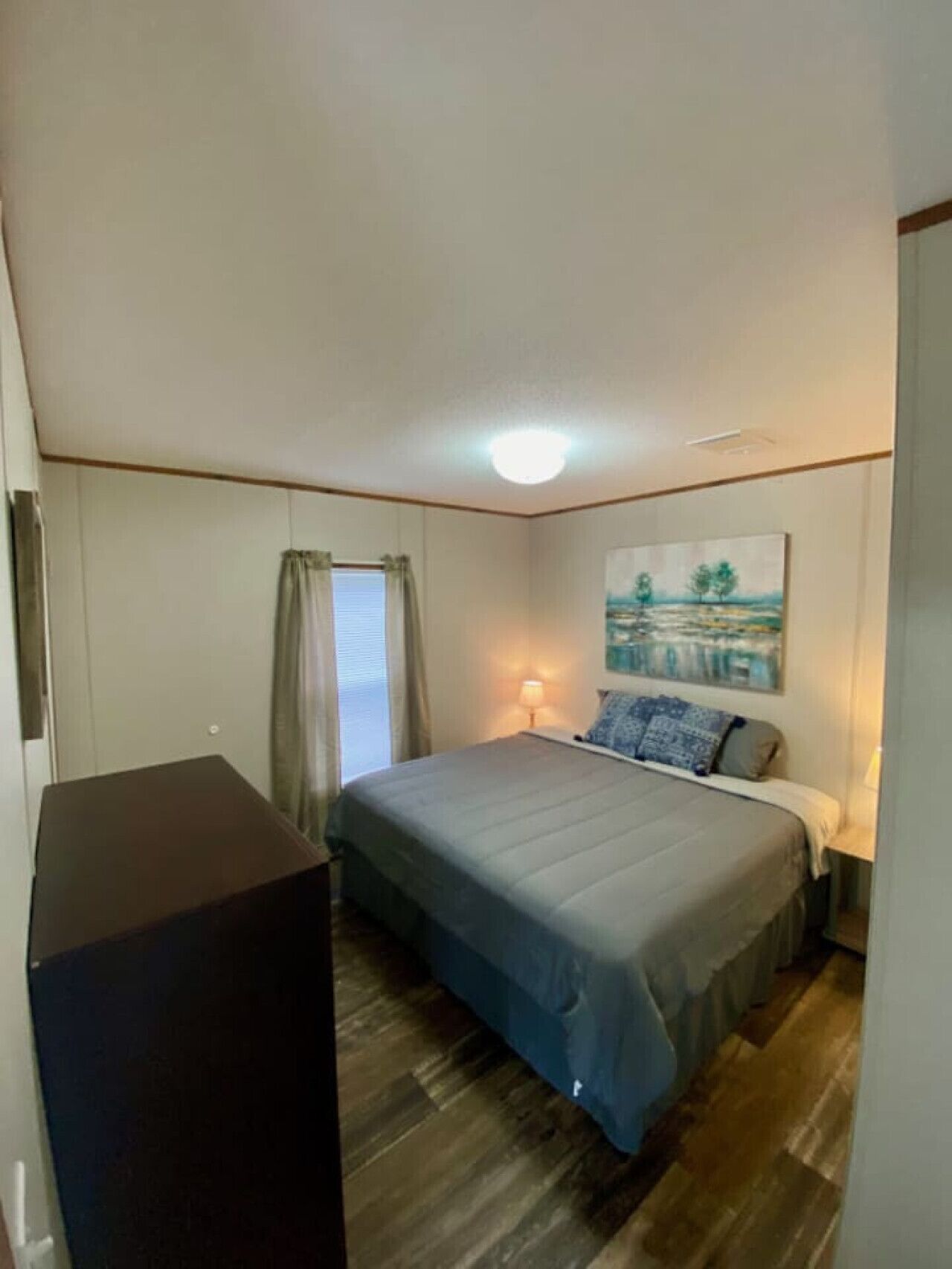 A bedroom with a bed, a desk, a lamp, and a painting on the wall.