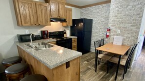 A kitchen with wooden cabinets, a granite countertop, a black refrigerator, a stove, and a dining table with chairs. - Rainbow River Bungalow Q (Dunnellon)