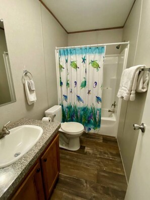 Een badkamer met een wastafel, toilet, badkuip en douchegordijn met afbeeldingen van zeedieren.