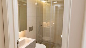 Een moderne badkamer met een douchecabine van glas, een witte wastafel en een toilet.