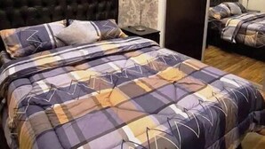 Quarto com cabeceira estofada, colcha estampada e espelho-armário.