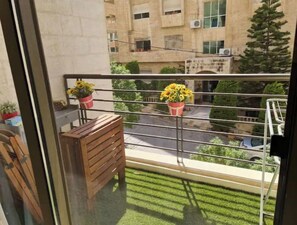 A balcony with two potted sunflowers, a wooden bench, and a view of a city street.