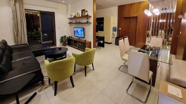 Uma sala de estar moderna com um sofá, duas poltronas amarelas, uma TV e uma área de jantar com mesa e cadeiras.