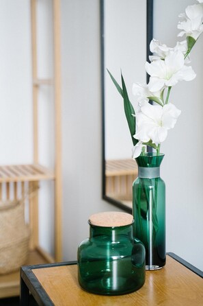 Un vase vert avec un bouchon en liège et un vase en verre, haut et étroit, doté d’une base en métal, tous deux placés sur une table en bois.