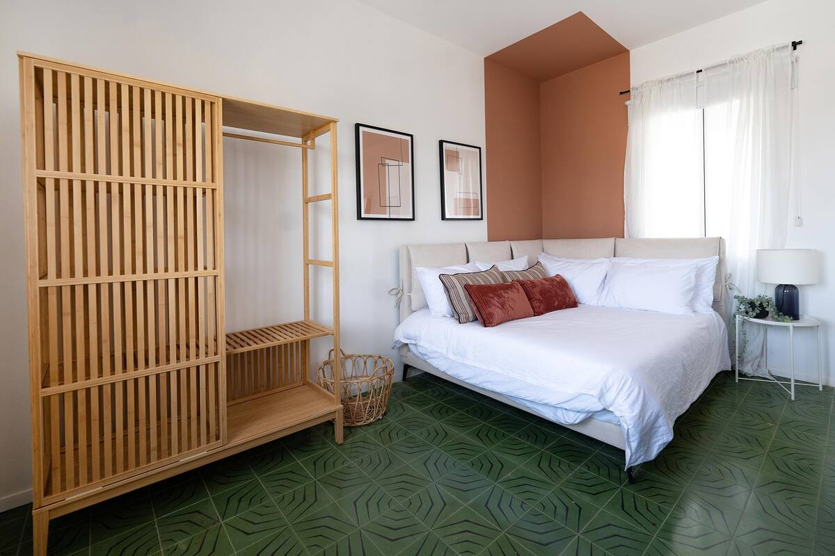 Une chambre à coucher avec un lit, une armoire en bois, une petite table avec une lampe et deux tableaux encadrés accrochés au mur.