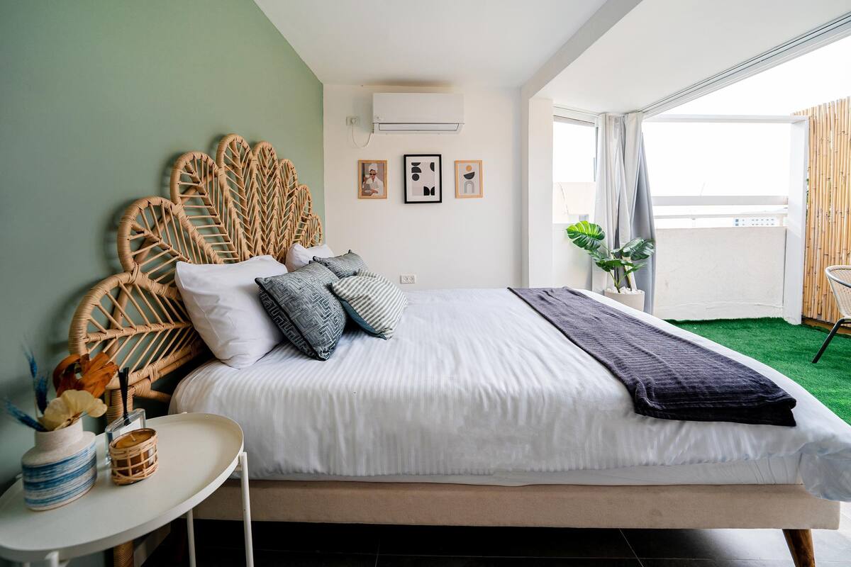 Une chambre à coucher comprenant un lit, une table de chevet, un climatiseur fixé au mur et une fenêtre donnant sur l’extérieur.