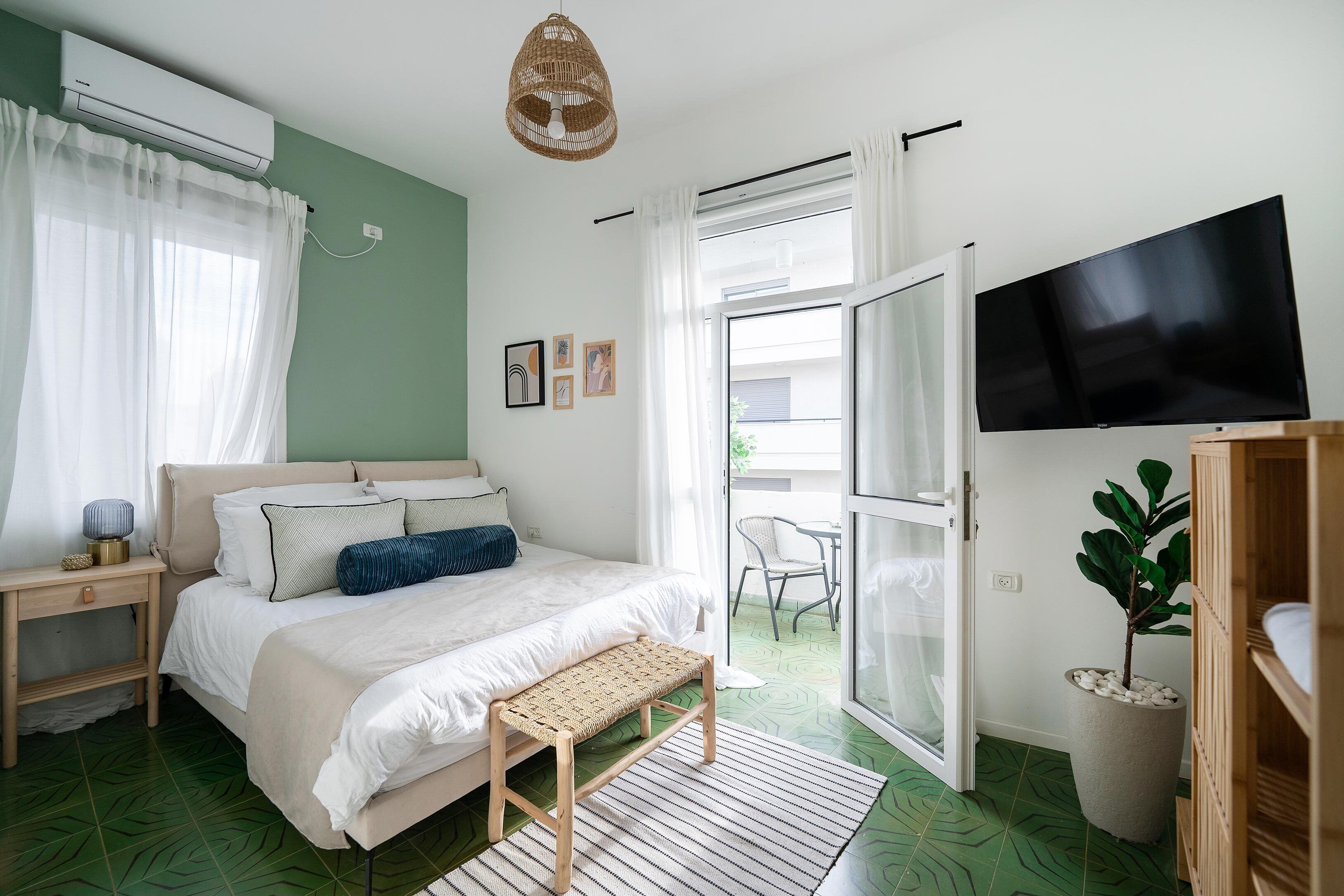 Une chambre à coucher comprenant un lit, une table de chevet, un banc, une télévision et une plante en pot.