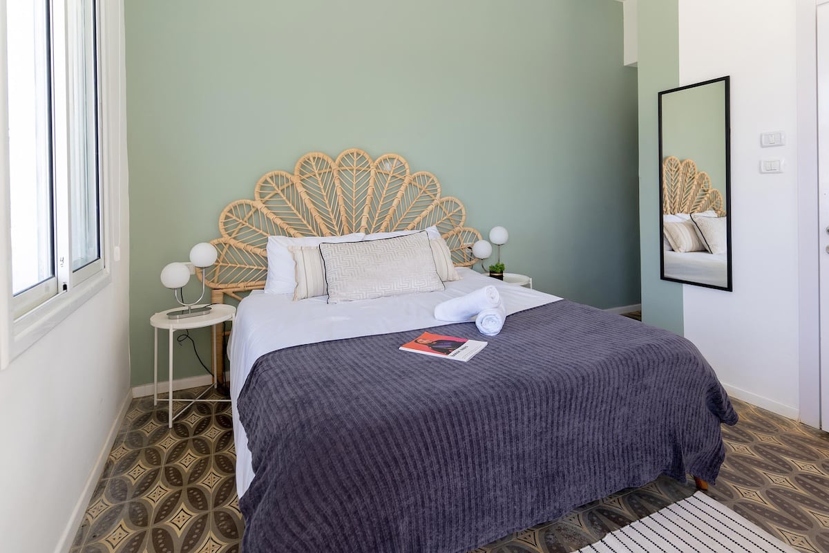 Un lit bien fait, avec une tête de lit à motifs, une lampe de chevet et une serviette enroulée posée sur le lit.