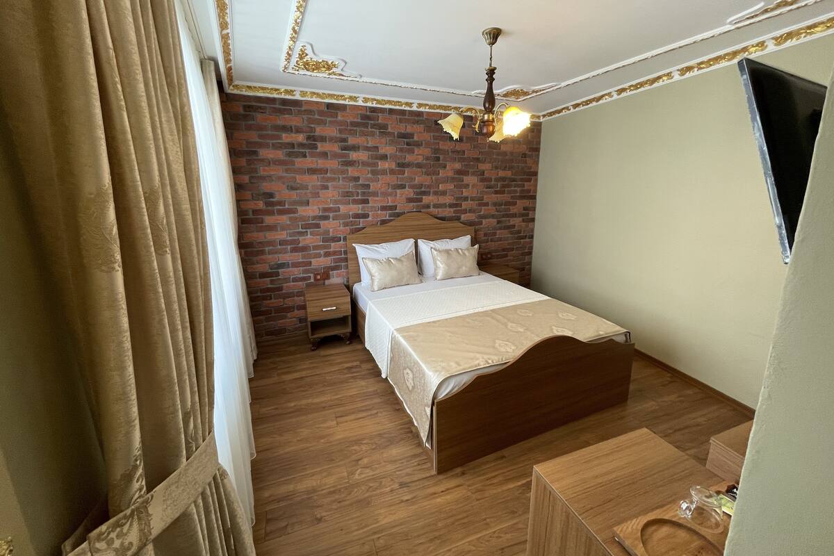 A bedroom with a wooden bed, a nightstand, a brick wall, and a ceiling fan.