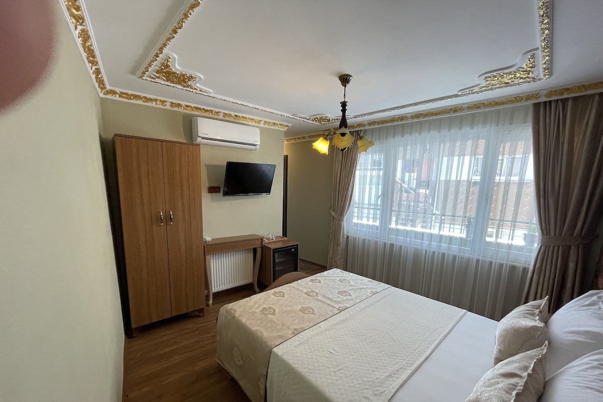 A hotel room with a bed, a desk, a television, and a window with curtains.