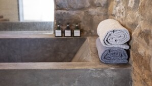 Una bañera de piedra con toallas dobladas y tres botellas de productos de baño.