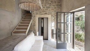 Un interior moderno con pared de piedra, una escalera, un sofá blanco y un ventanal con vistas a zonas verdes.