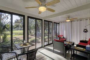 A sunroom with large windows, wicker furniture, ceiling fans, and a view of a park. - 2 BR Lagoon & Golf Views Walk to Ocean King 2 Twins Bikes & Beach Gear included (Hilton Head Island)