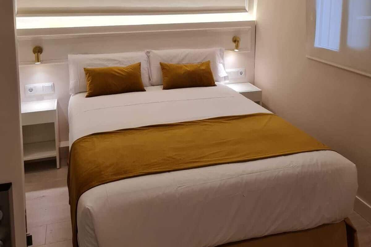 A modern bedroom with a large bed, bedside tables, and a headboard with integrated lighting.