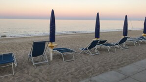 En strand med rader av solstolar och parasoller, ett lugnt hav och en klar himmel.