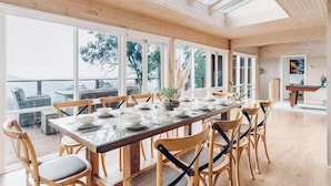A spacious dining area with a long table set for six, wooden chairs, and large windows offering a view of the sea. - Villa with Spa and Breathtaking Views of Dandenong Ranges (Kalorama)