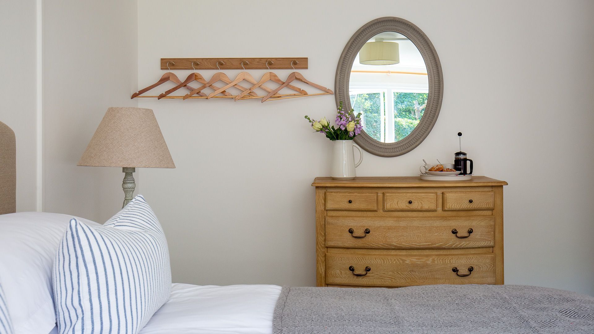 A bedroom with a bed, a dresser, a mirror, a lamp, and a wall-mounted coat rack.