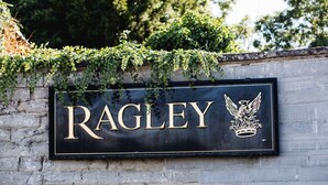 A sign with the name "RAGLEY" and an emblem, mounted on a stone wall with ivy growing over it.