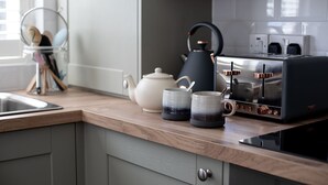 A kitchen with a modern design, featuring a stainless steel toaster, a white teapot, and two ceramic mugs.