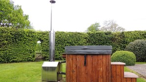 A wooden outdoor structure with a metal base, possibly a barbecue or storage unit, in a well-maintained garden with a hedge and a street lamp in the background.