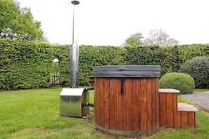 A wooden outdoor structure with a metal base, possibly a barbecue or storage unit, in a well-maintained garden with a hedge and a street lamp in the background.