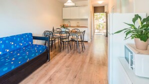 Un espace de vie compact comprenant un canapé, une table à manger, des chaises, un coin cuisine et un réfrigérateur.