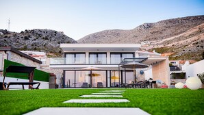 Una casa moderna de dos pisos con un balcón, un patio con mobiliario exterior y un césped bien cuidado.