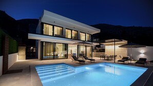 Una casa moderna de dos pisos con piscina, mobiliario exterior y un patio bien iluminado.