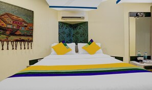 Habitació d'hotel amb un llit, un tapís mural, un aire condicionat i una taula de nit amb una ampolla.