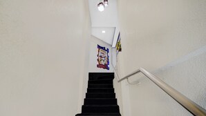 Eine Treppe mit Handlauf, eine Wand mit einem Plakat und eine Deckenleuchte.