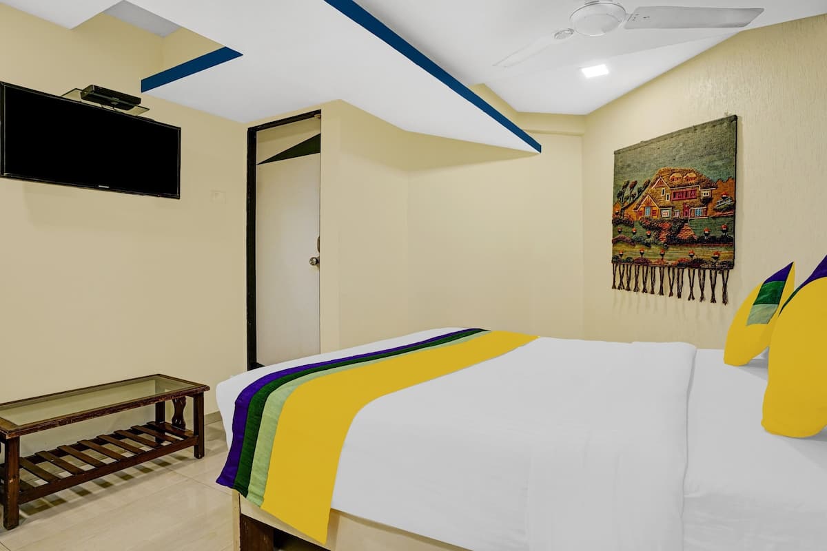 A bedroom with a bed, a TV mounted on the wall, a door, and a painting.