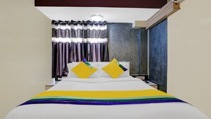 Ein Hotelzimmer mit einem Bett, zwei Kissen, einem Nachttisch und einem Fenster mit Vorhängen.