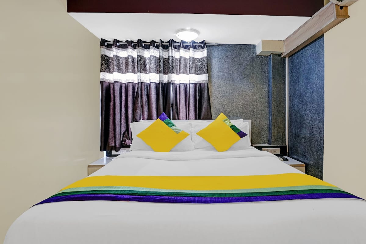 A hotel room with a bed, two pillows, a nightstand, and a window with curtains.