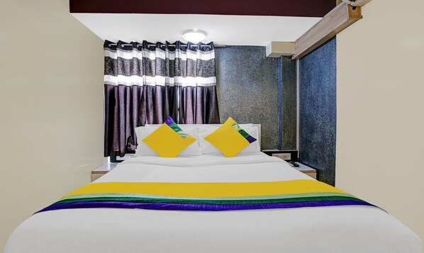 A hotel room with a bed, two pillows, a nightstand, and a window with curtains. - Hotel Amber Corp Inn (Mumbai)