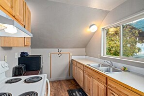 Une cuisine compacte avec des meubles en bois, une cuisinière blanche, un évier et une fenêtre donnant sur les arbres.