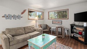 A living room with a sofa, a coffee table, a lamp, a TV, and a bookshelf. - Downtown Leavenworth | King Bed + Parking (Leavenworth)
