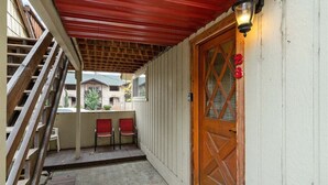 A covered porch with a wooden staircase, a wooden door with a number, and two red chairs. - Downtown Leavenworth | King Bed + Parking (Leavenworth)