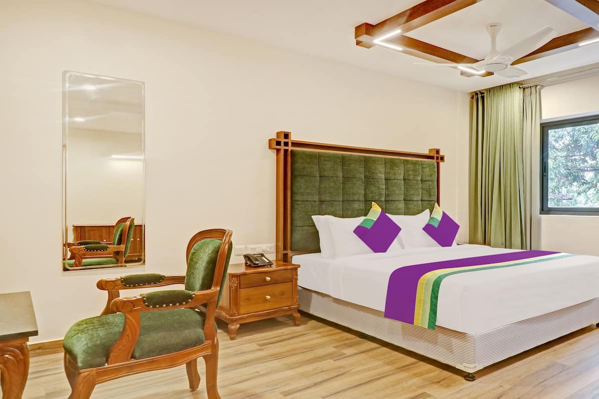 Quarto de hotel com uma cama grande, mesas de cabeceira de madeira, uma escrivaninha e cadeiras.