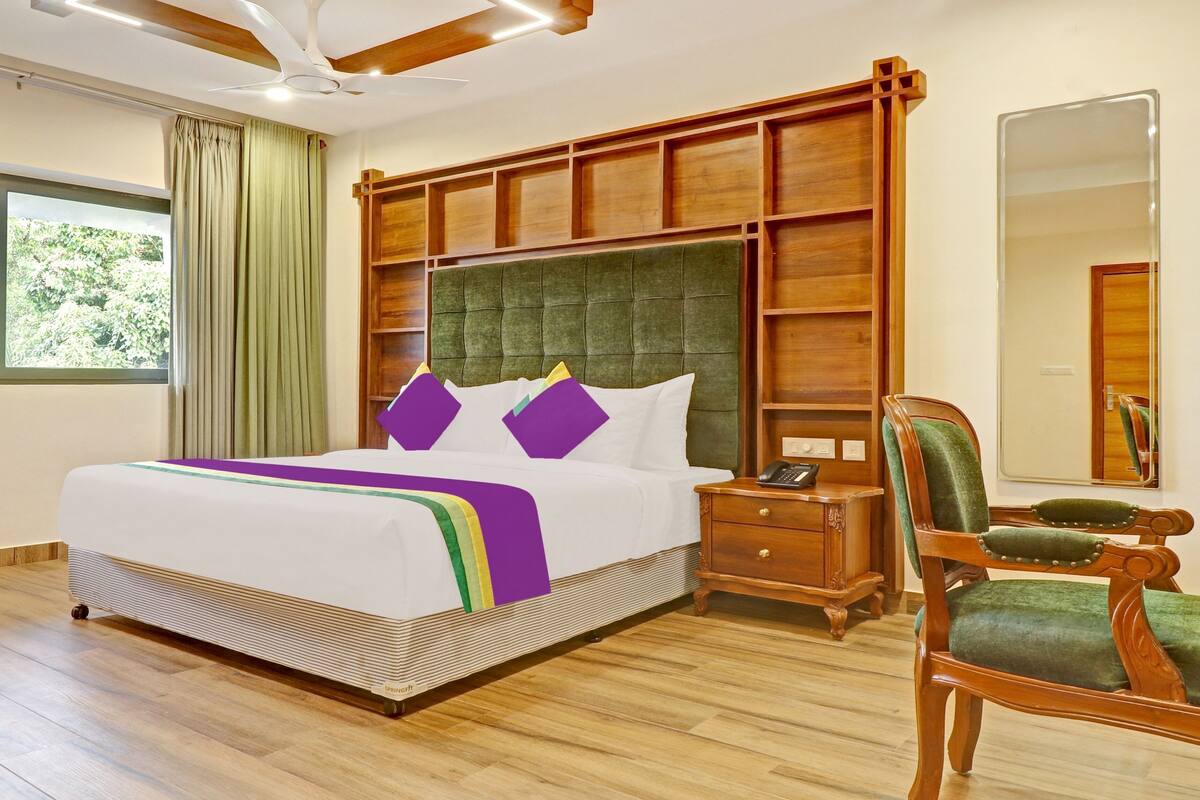 Quarto de hotel com uma cama grande, cabeceira de madeira, mesa de cabeceira, uma cadeira e um espelho.