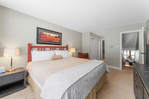 Une chambre d’hôtel avec un grand lit, deux tables de chevet avec des lampes, un tableau au-dessus du lit, une armoire et une porte donnant sur une salle de bain.