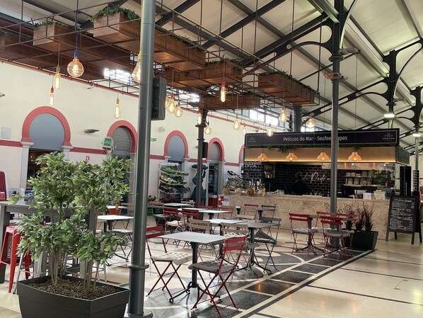 Un espace de restauration intérieur avec des tables et des chaises, un comptoir où est affiché le menu, et des luminaires suspendus.