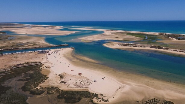 Una vista aerea di una zona costiera con spiaggia, acque blu cristalline e una costa in lontananza.